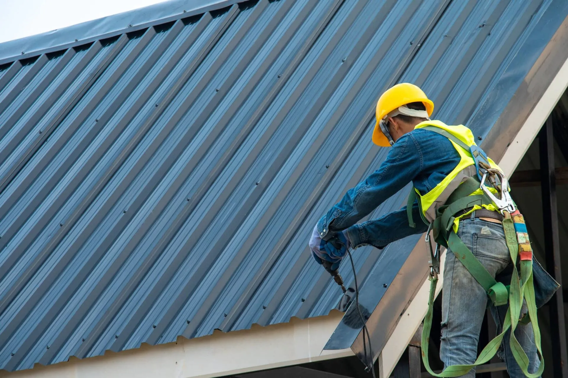 Roofing contractor installing standing seam metal roofing panels, securing metal flashing and fasteners with proper fall protection.